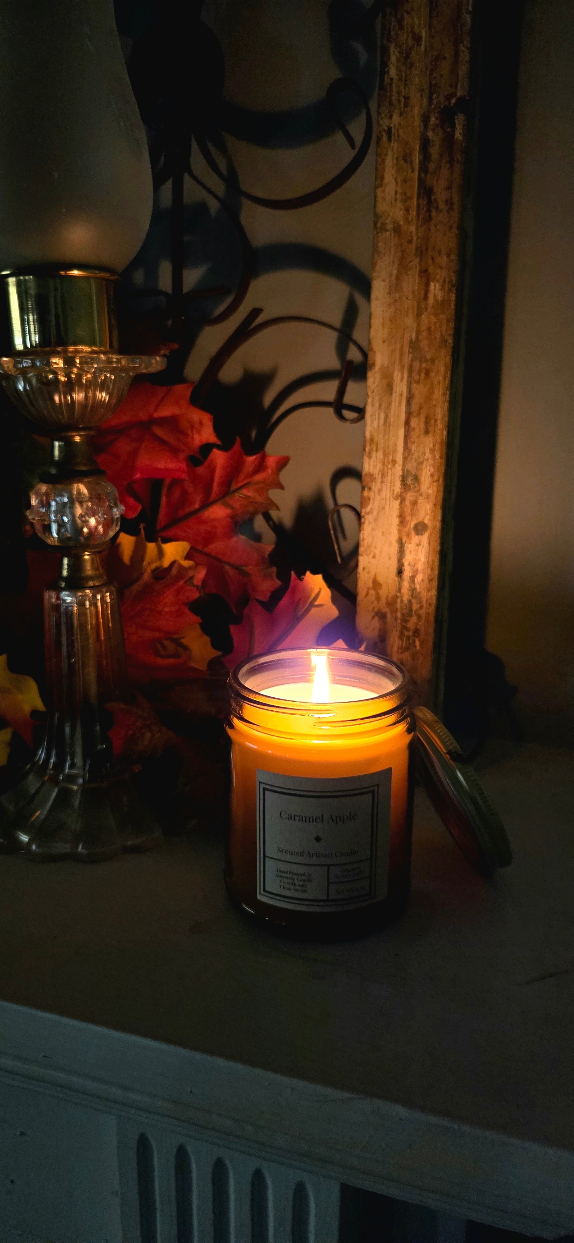 Candle with a label on a surface, surrounded by decorative items in a dimly lit room.