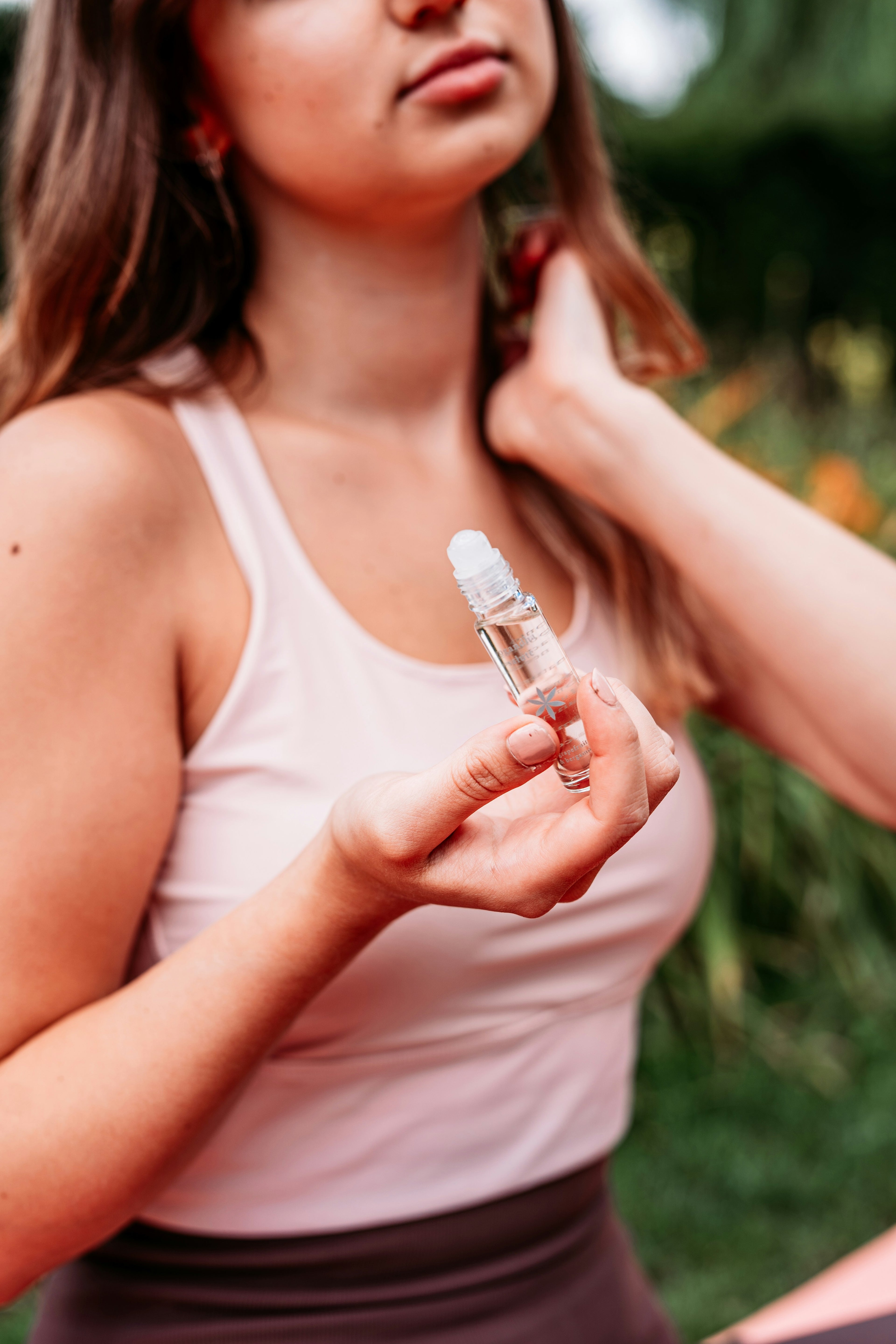 Woman holding a small essential oil bottle outdoors with a blurred natural background