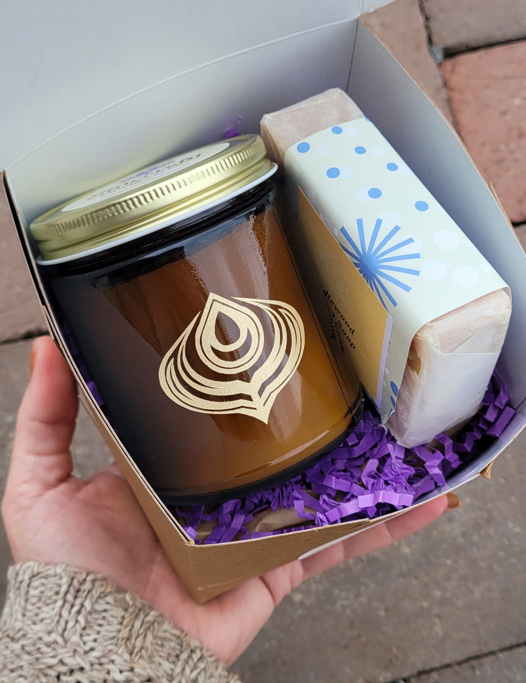 Hand holding a gift box with a jar and a bar of soap inside