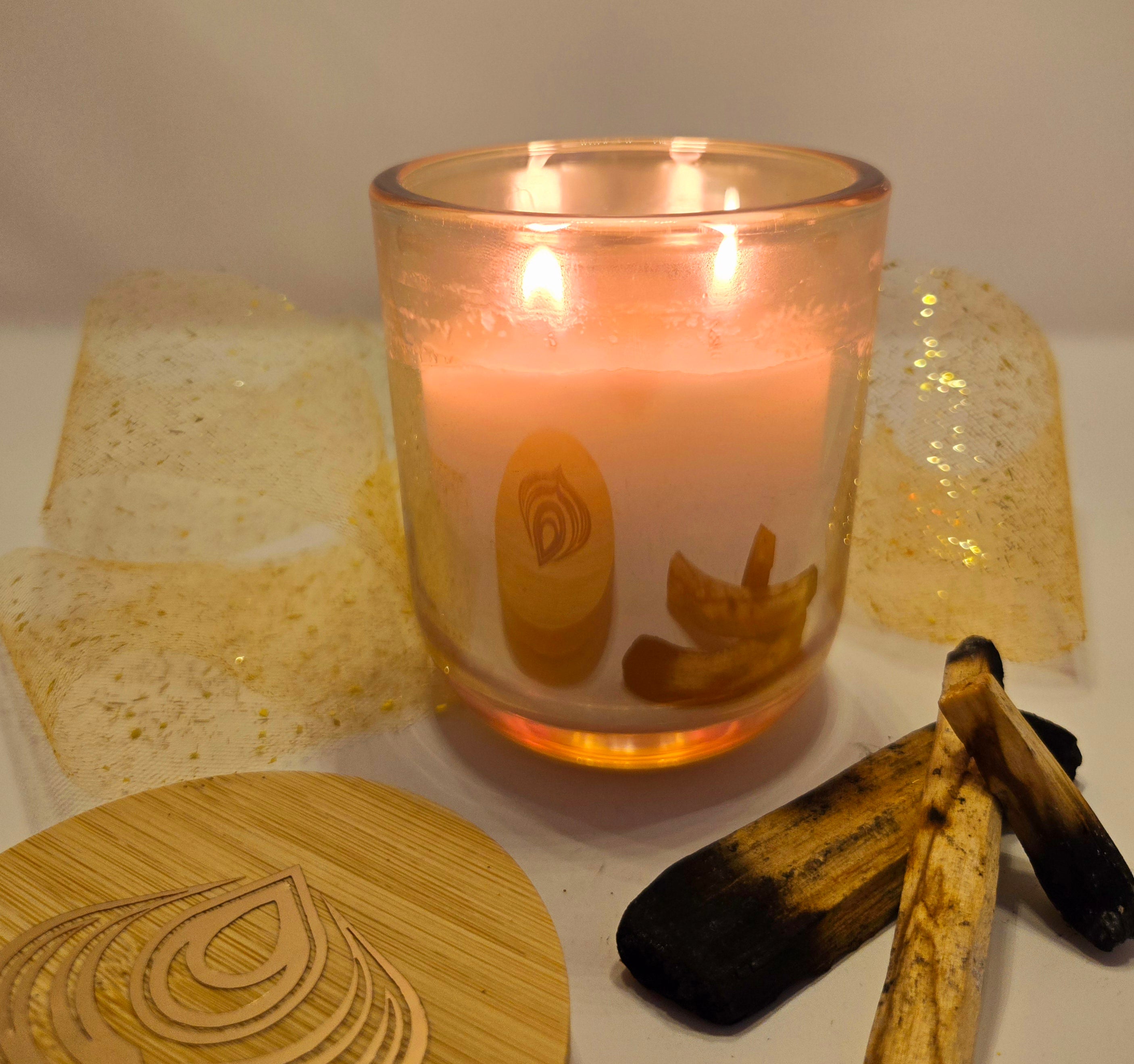 A lit scented candle with a velour texture, surrounded by wooden elements and a decorative coaster, suggesting a warm and intimate ambiance.
