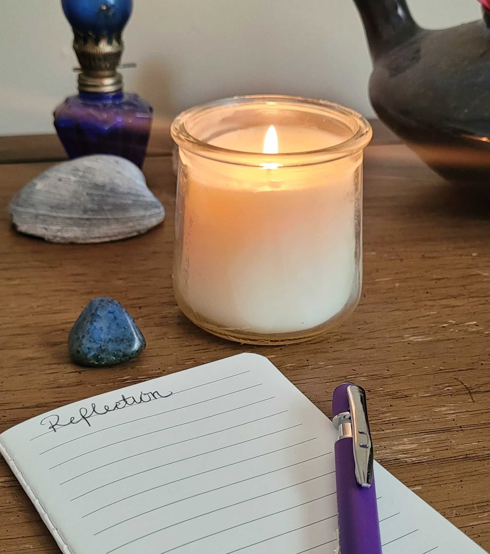 candle burning on table next to a reflection journal and pen