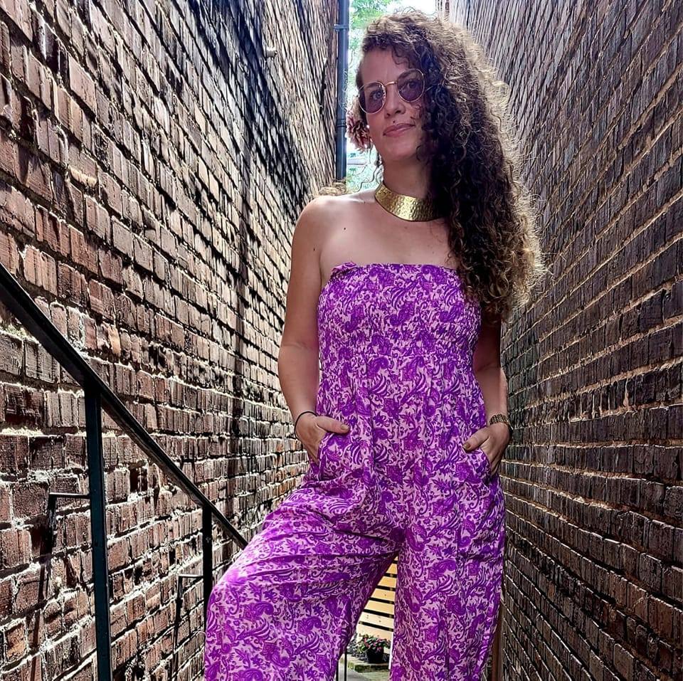 Kimberly Powers, owner of Alchemia LLC, standing in a brick alley, wearing a pink jumpsuit