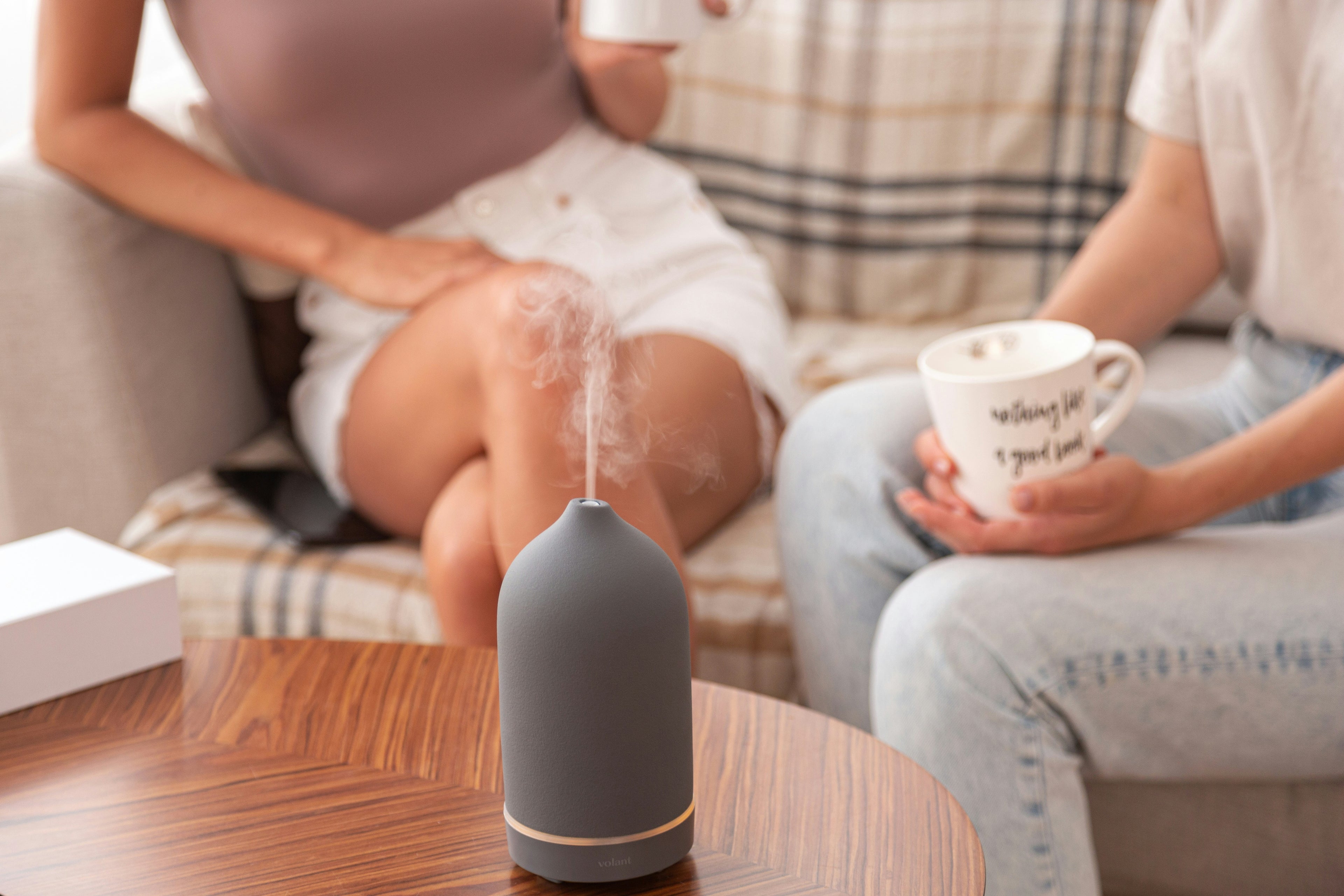 Two people sitting on a couch with a diffuser and cups on a table in front of them.