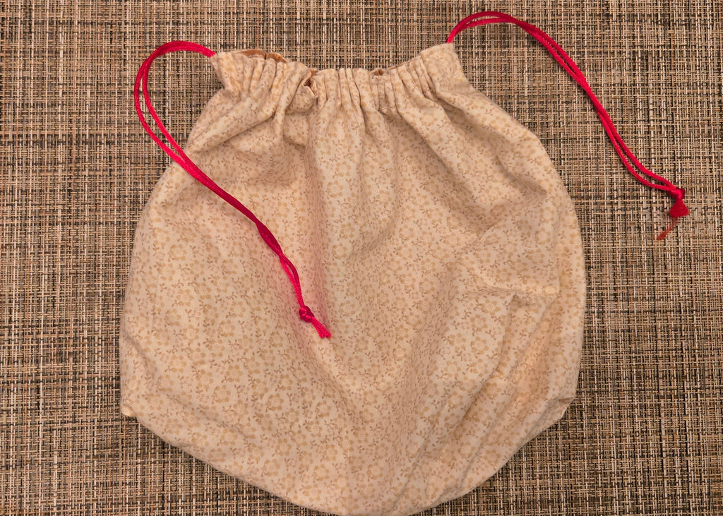 Beige drawstring bag with red string on a textured surface