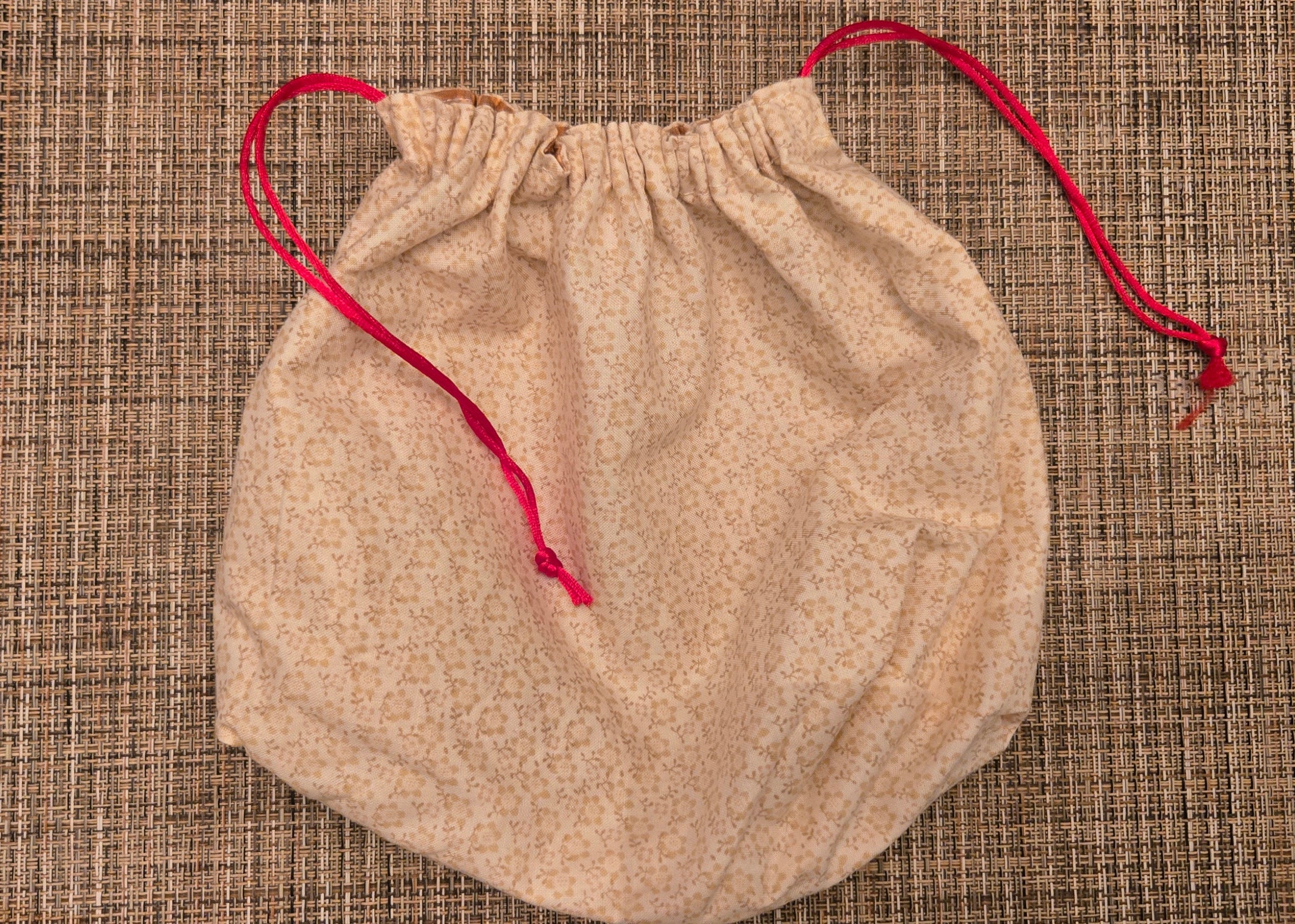 Beige drawstring bag with red string on a textured surface
